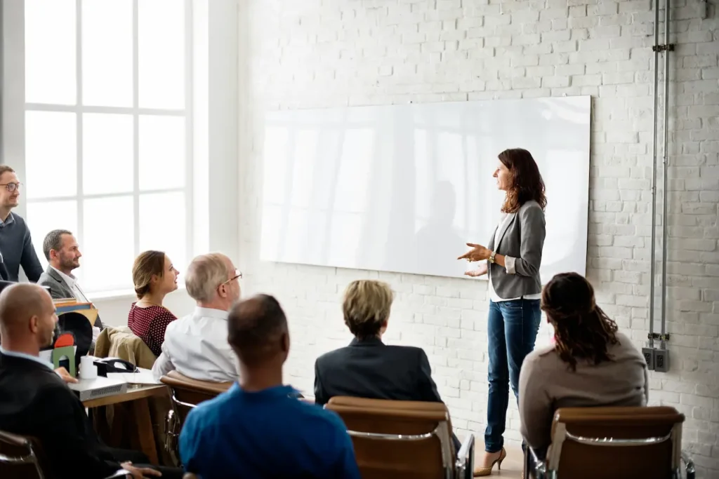 Dirigeante devant un tableau blanc présentant les priorités retenues à un groupe assis